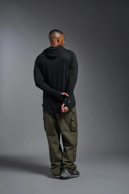 Person wearing a black hoodie and green pants against a gray background