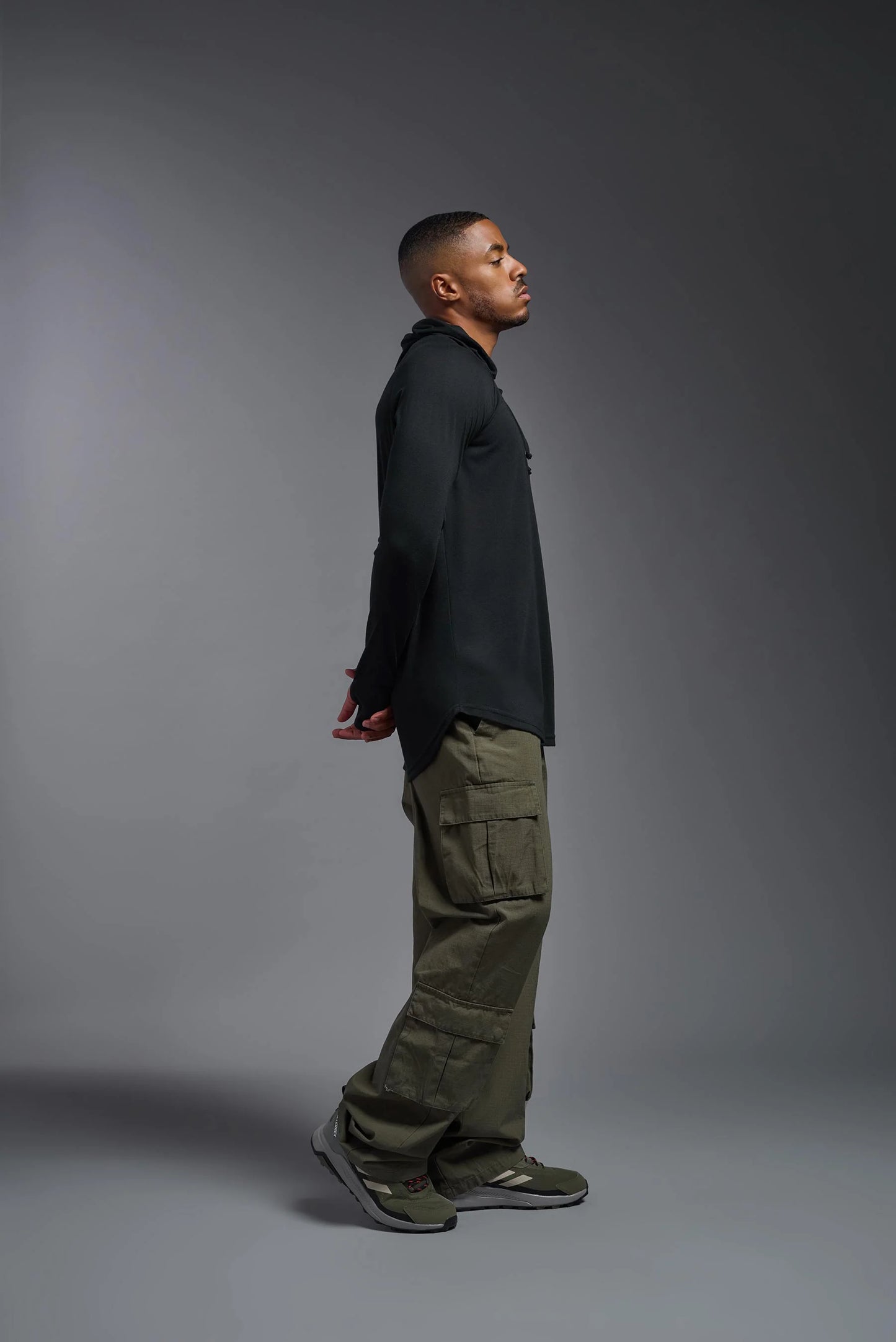 Man wearing a black long-sleeve shirt and green cargo pants standing against a gray background