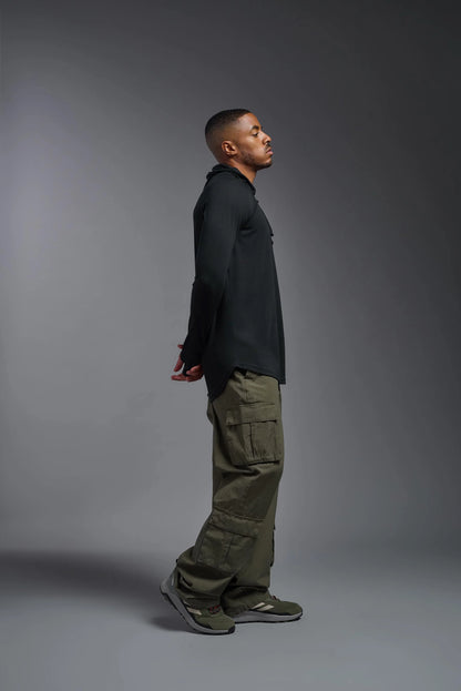 Man wearing a black long-sleeve shirt and green cargo pants standing against a gray background