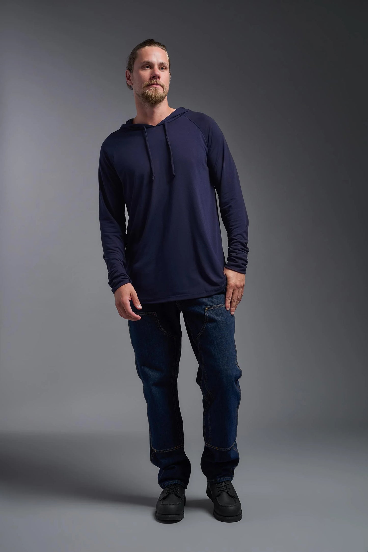 Man wearing a navy long-sleeve shirt and dark jeans against a gray background
