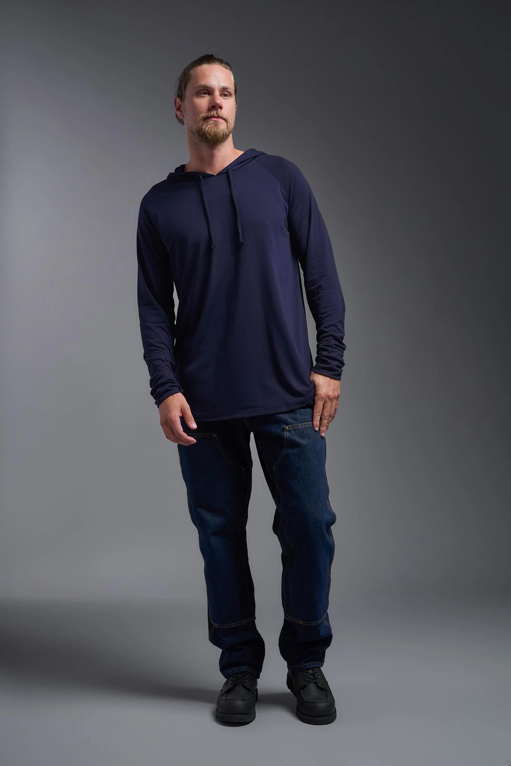 Man wearing a navy long-sleeve shirt and dark jeans against a gray background