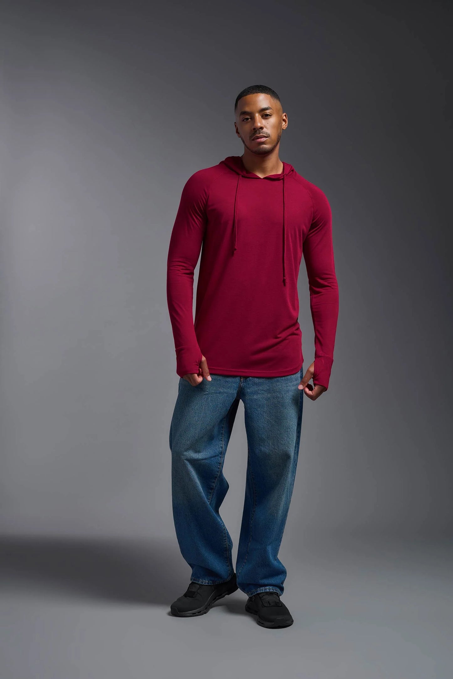 Man wearing a red long-sleeve shirt and blue jeans against a gray background