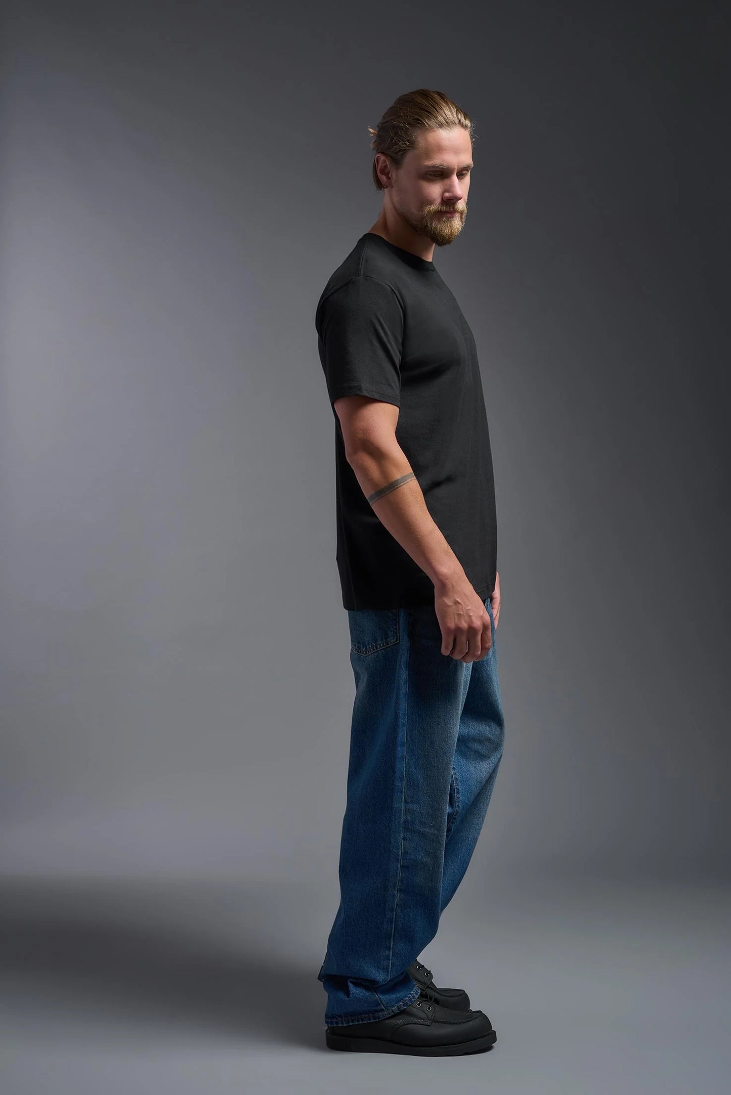 Man wearing a black t-shirt and blue jeans standing against a gray background
