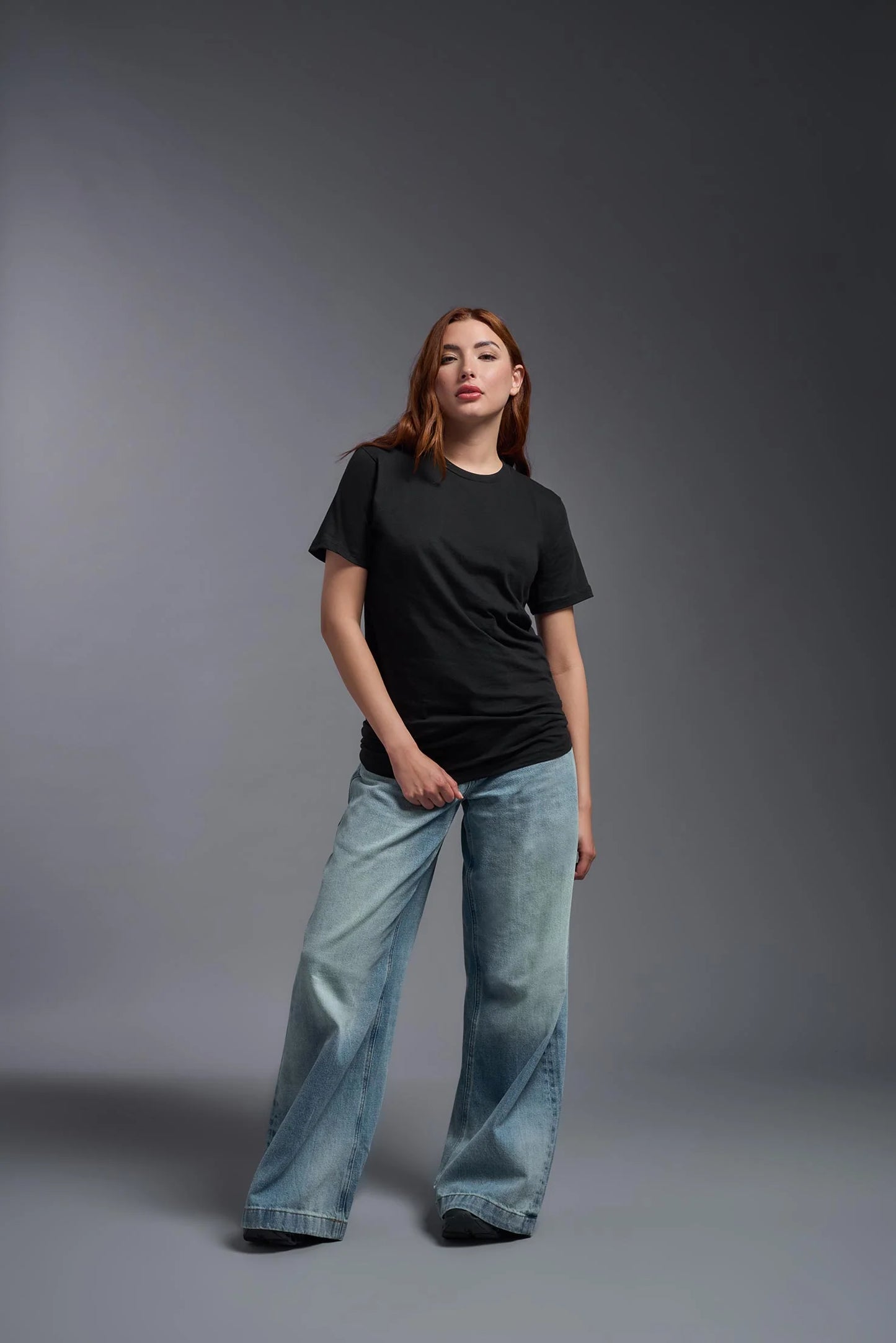 Woman wearing a black t-shirt and light blue jeans against a gray background