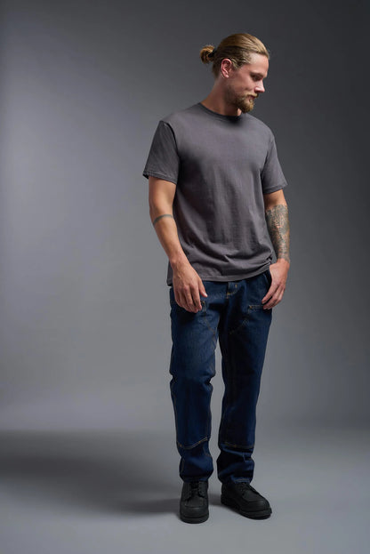 Man wearing a gray t-shirt and blue jeans standing against a gray background