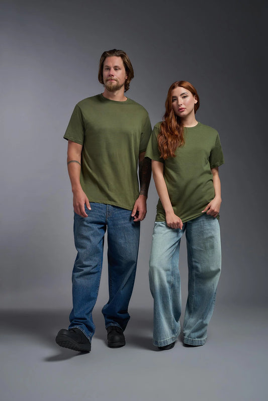 Two people wearing green t-shirts and blue jeans standing against a gray background