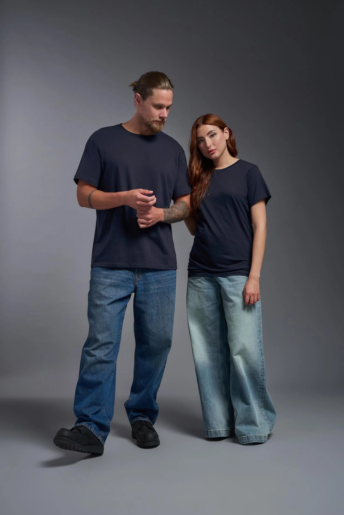 Two people wearing matching dark blue t-shirts and light blue jeans on a gray background