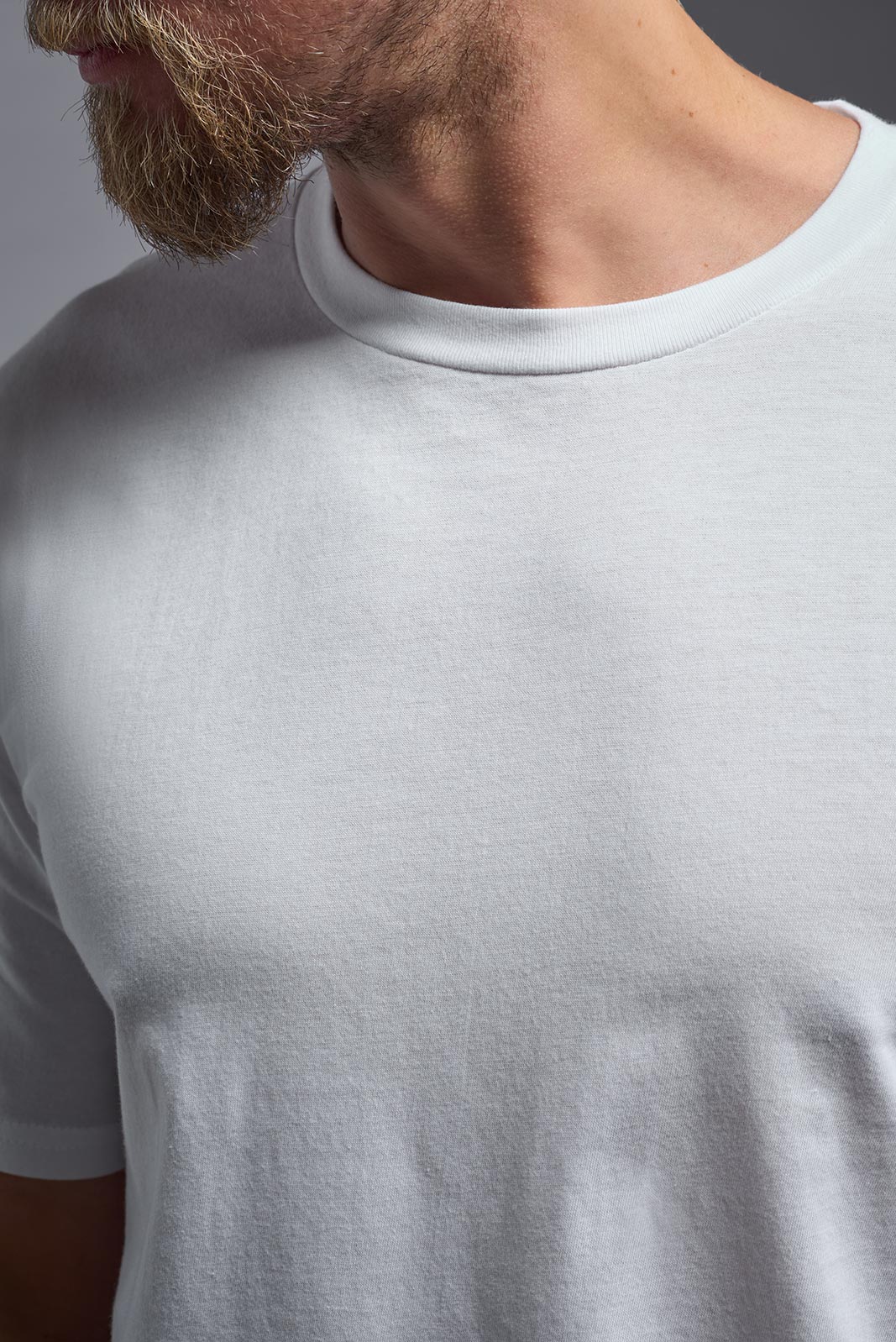 Close-up of a person wearing a plain white t-shirt against a neutral background