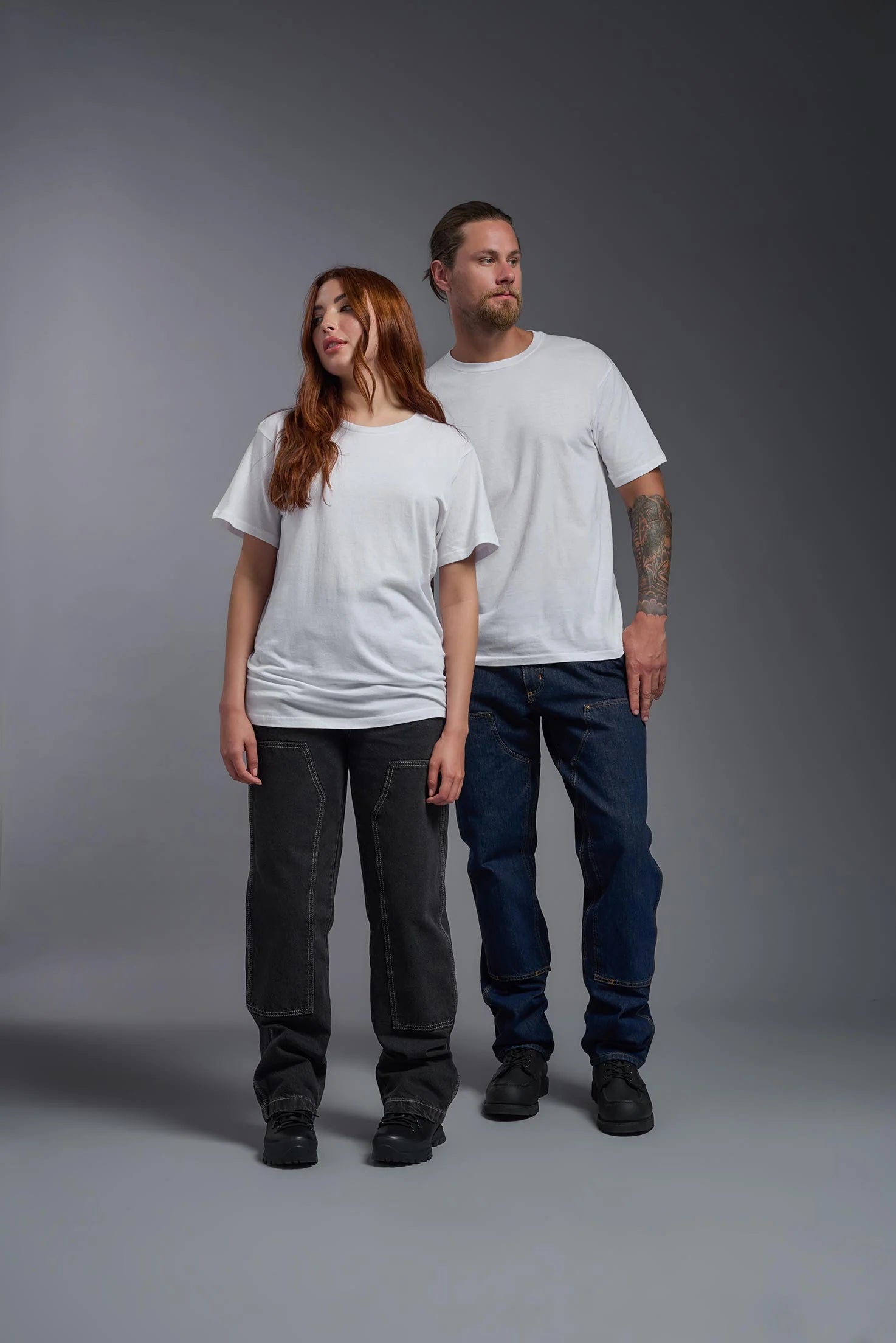 Two people wearing plain white t-shirts and dark pants against a gray background