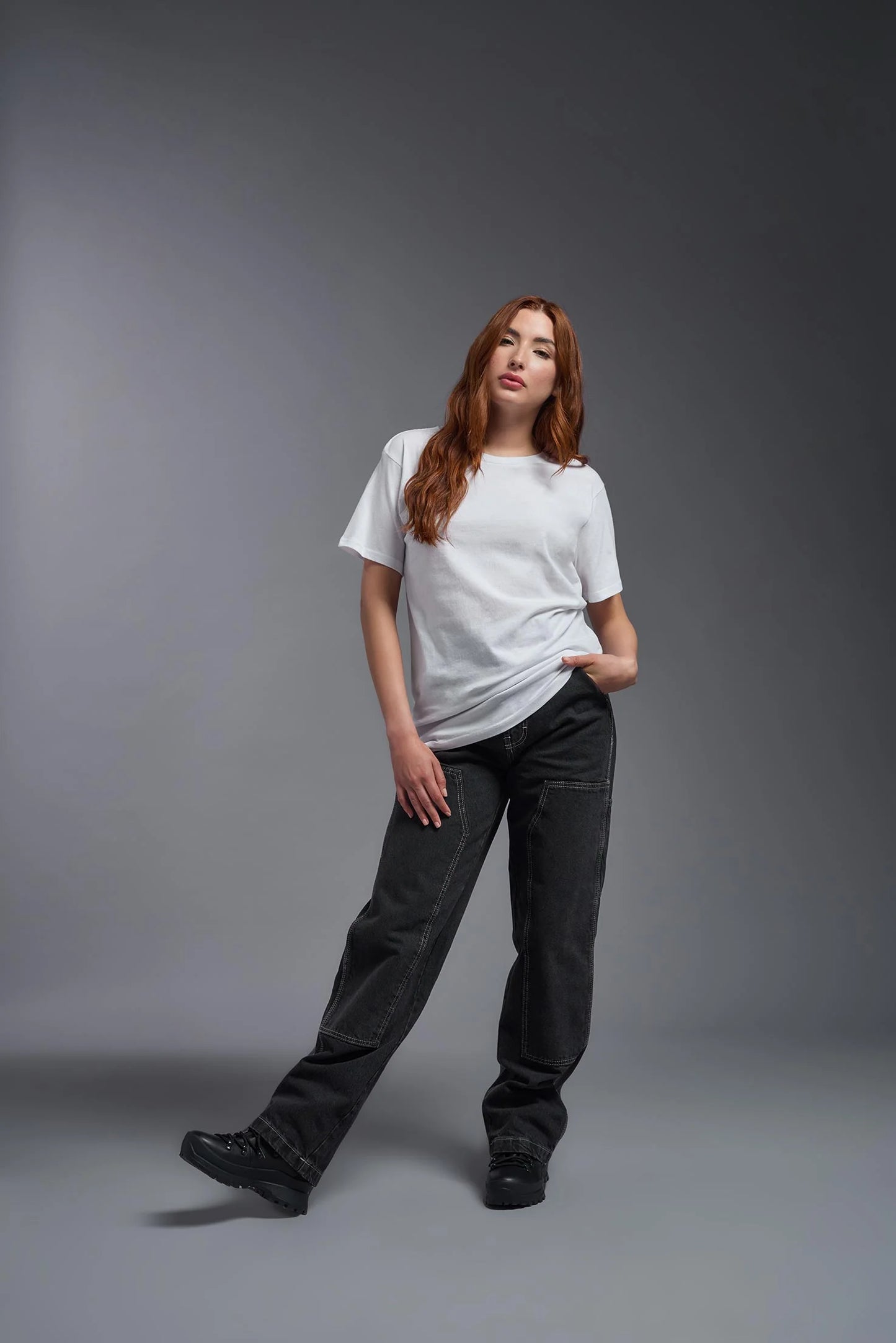 Woman wearing a white t-shirt and dark jeans against a gray background