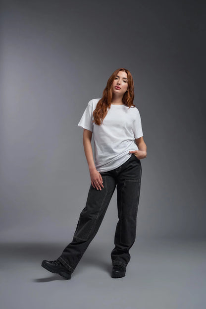 Woman wearing a white t-shirt and dark jeans against a gray background