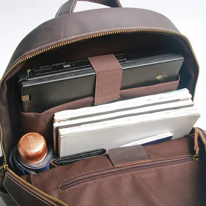 Brown backpack with items including a laptop, notebooks, and a coffee cup.