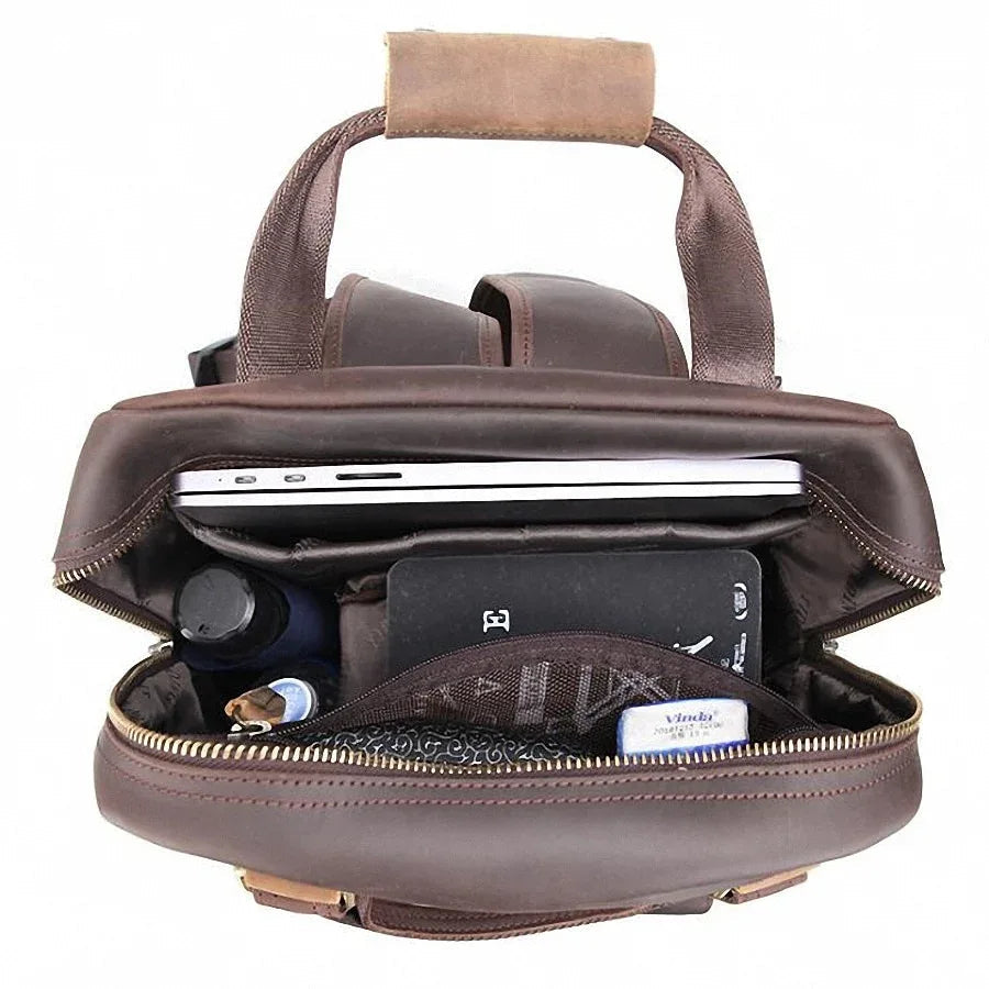Brown leather camera backpack open at top, showing padded camera compartments and zipper closure