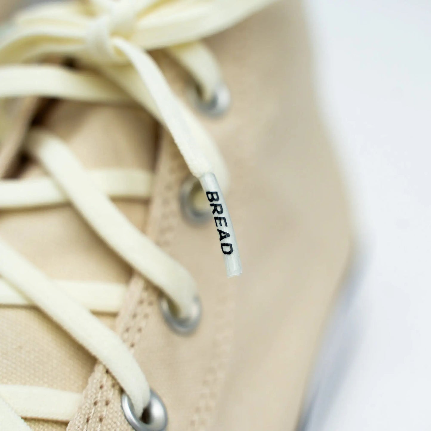 Close-up of beige sneaker with white laces and a visible brand tag.