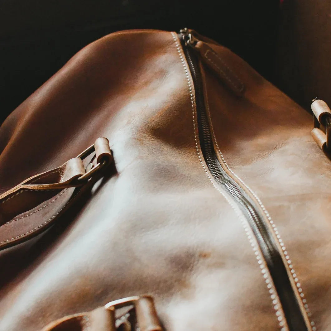 Brown leather duffle bag close-up of smooth panel and zipper track with stitching.