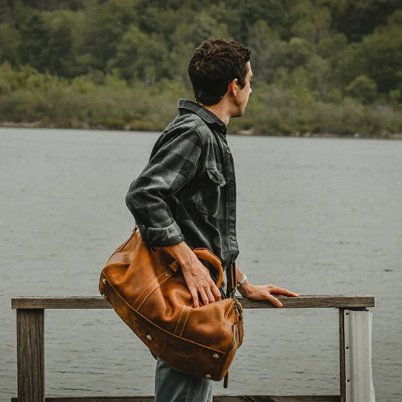 Brown leather duffle travel bag with top handles, front zip pocket, and sturdy carry straps.