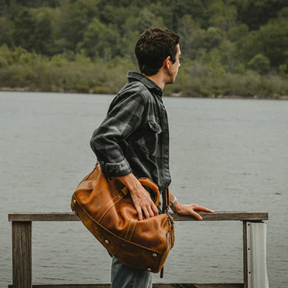 Brown leather duffle travel bag with top handles, front zip pocket, and sturdy carry straps.
