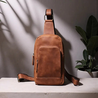 Brown leather crossbody sling bag standing with front pocket and adjustable strap