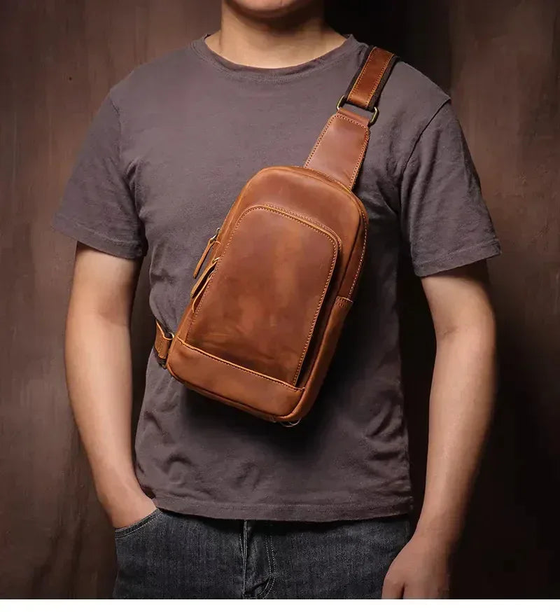 Brown leather crossbody sling bag worn across chest with front zipper pocket
