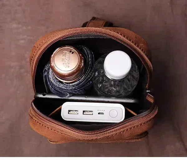 Brown leather crossbody bag open with zipper compartment holding small electronics