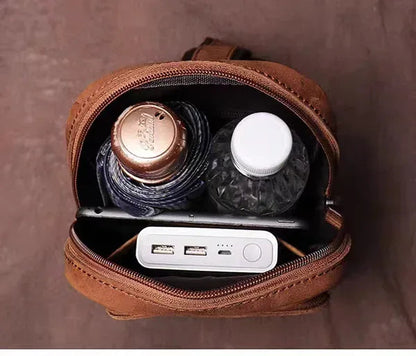 Brown leather crossbody bag open with zipper compartment holding small electronics