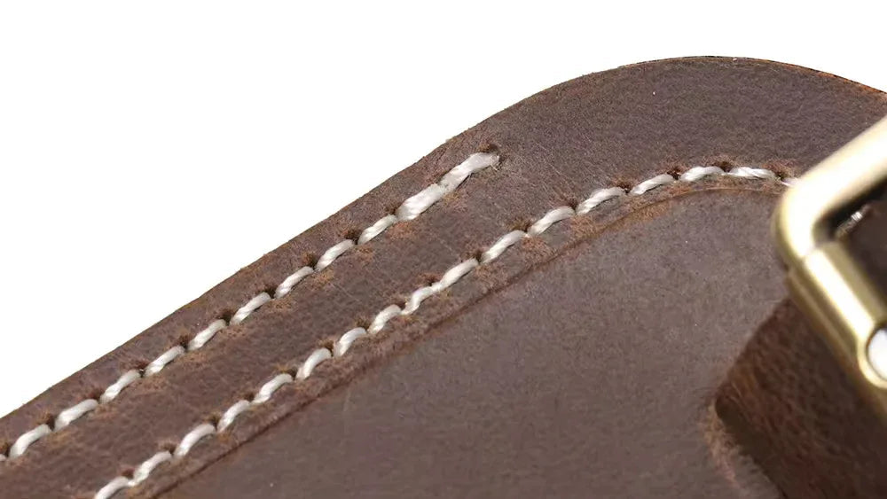Close-up of dark brown leather luggage tag stitching near metal buckle hardware.