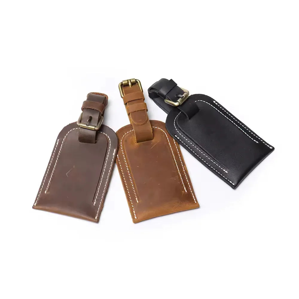 Leather luggage tags with metal buckles in black, brown, and dark brown with stitching.