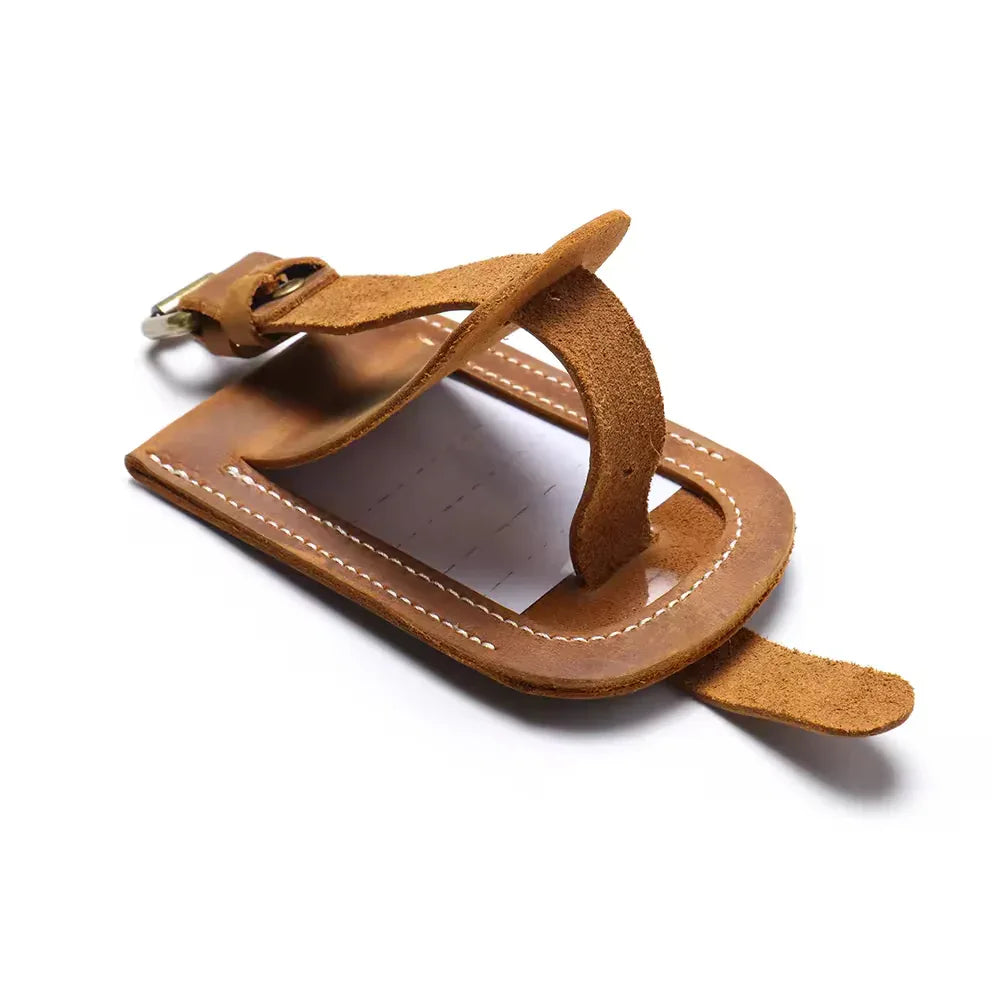 Tan leather luggage tag with metal buckle and stitched border on a leather loop.