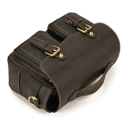 Dark brown leather camera bag with stitched panels and buckle closures on the top flap