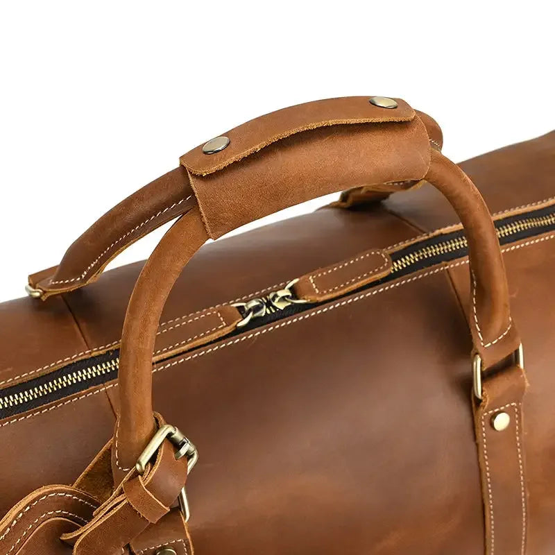Brown leather duffle bag close-up of top handle and strap hardware with zipper edge.