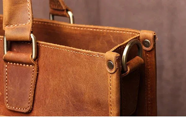 Brown leather messenger bag top handle with metal grommets on side panel