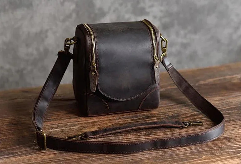 Small brown leather camera bag with shoulder strap and front flap, brass hardware.