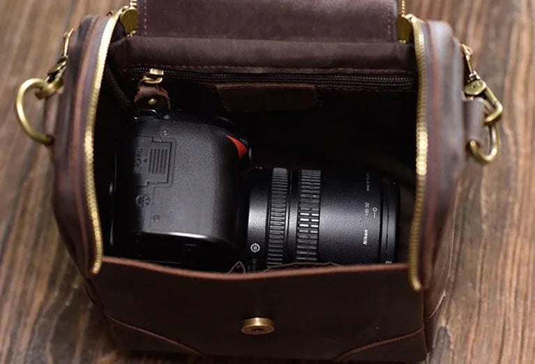 Small leather camera bag with open top showing camera and lens compartments inside.