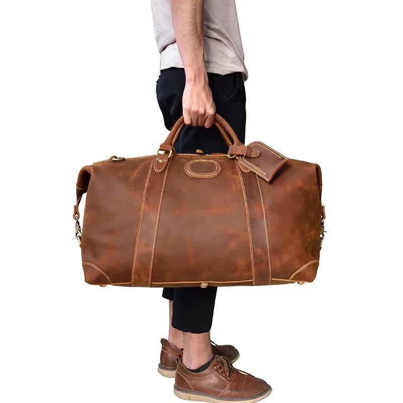 Vintage leather duffle bag carried by hand, brown color, with detachable strap.