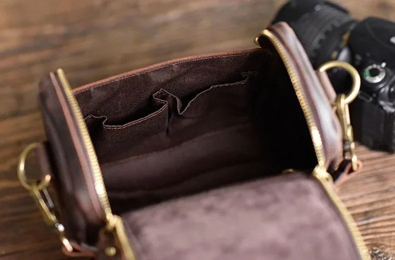 Small leather camera bag open, showing interior compartments and stitch-lined dividers.