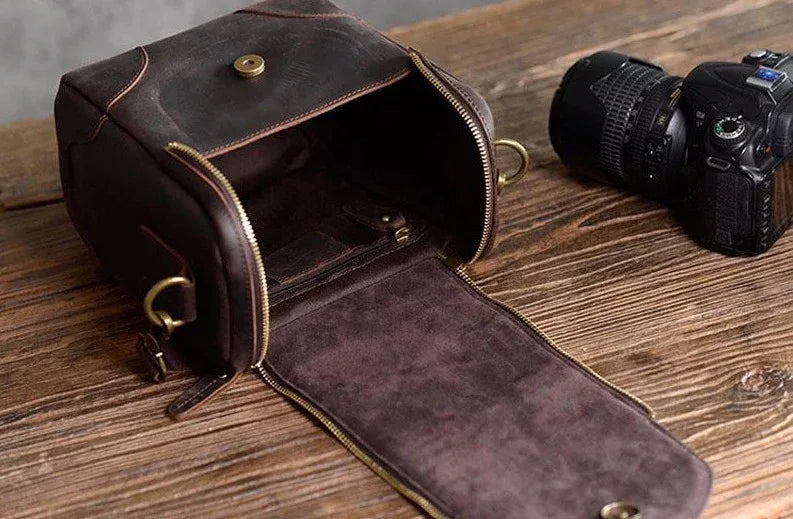 Small leather camera bag open to reveal lined interior and front zip closure, brass rings.