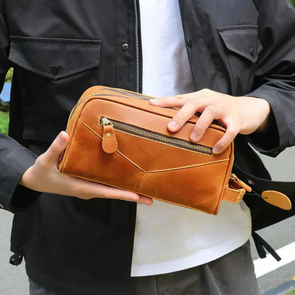 Tan leather toiletry bag held by a hand; front zip pocket and metal hardware