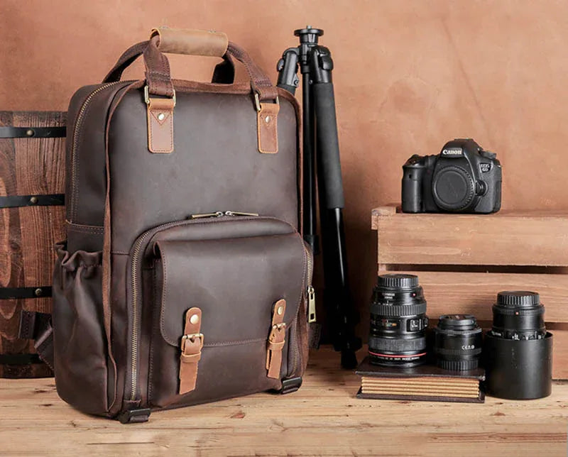 Dark brown leather camera backpack with tripod and camera lenses displayed nearby
