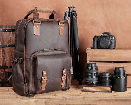 Dark brown leather camera backpack with tripod and camera lenses displayed nearby
