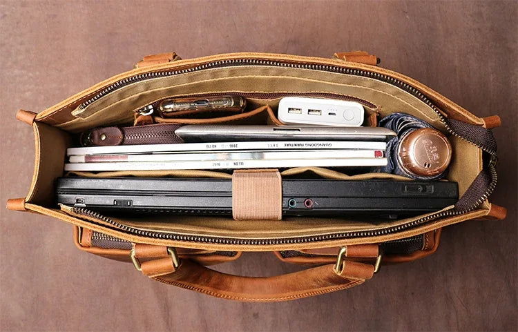 Brown leather messenger bag interior with notebooks and devices in a zippered compartment
