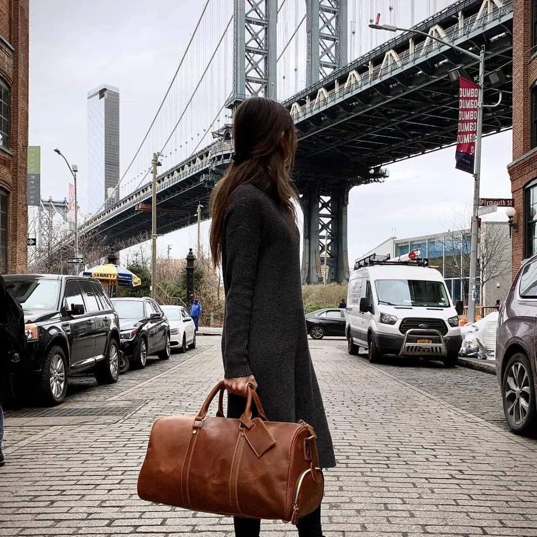 Brown leather duffle travel bag with top handles and a diamond-shaped front leather patch.