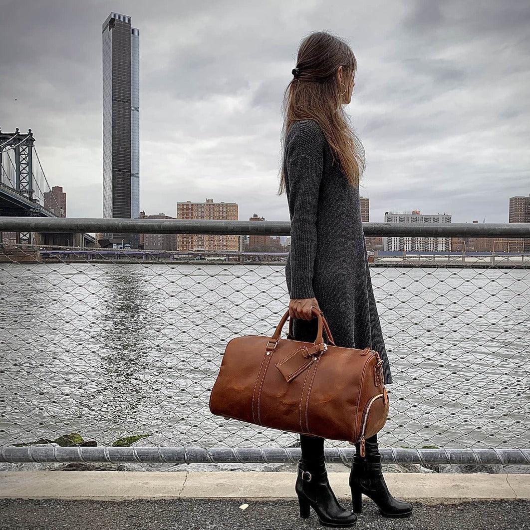 Brown leather duffle travel bag with metal rivets, stitched panels, and top handles.