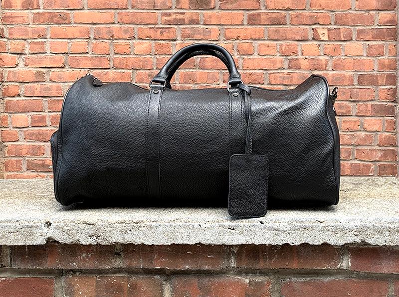 Black vintage leather weekender duffle bag with front zipper and hanging luggage tag