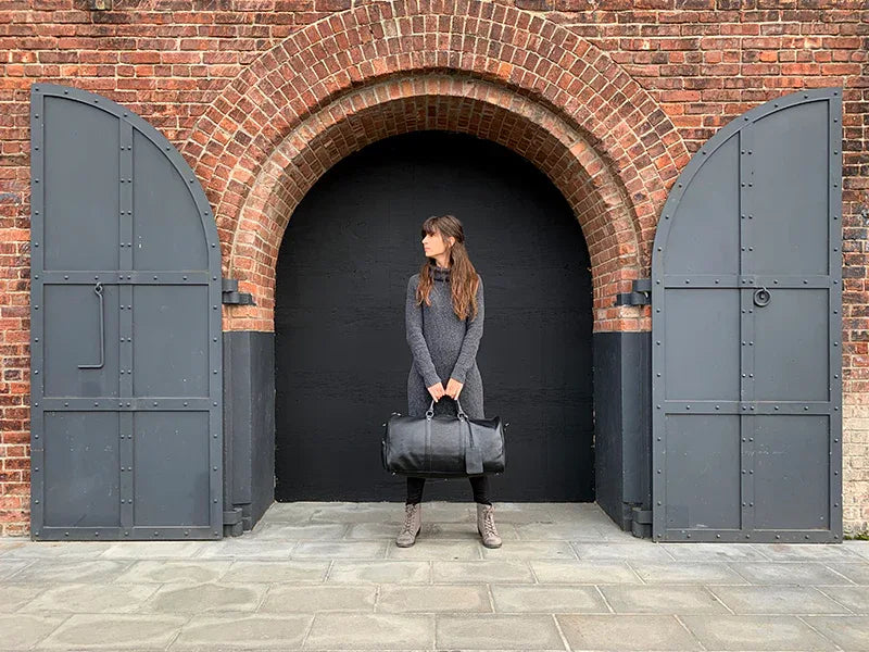 Black vintage leather weekender duffle bag with top handles, carried by the shopper