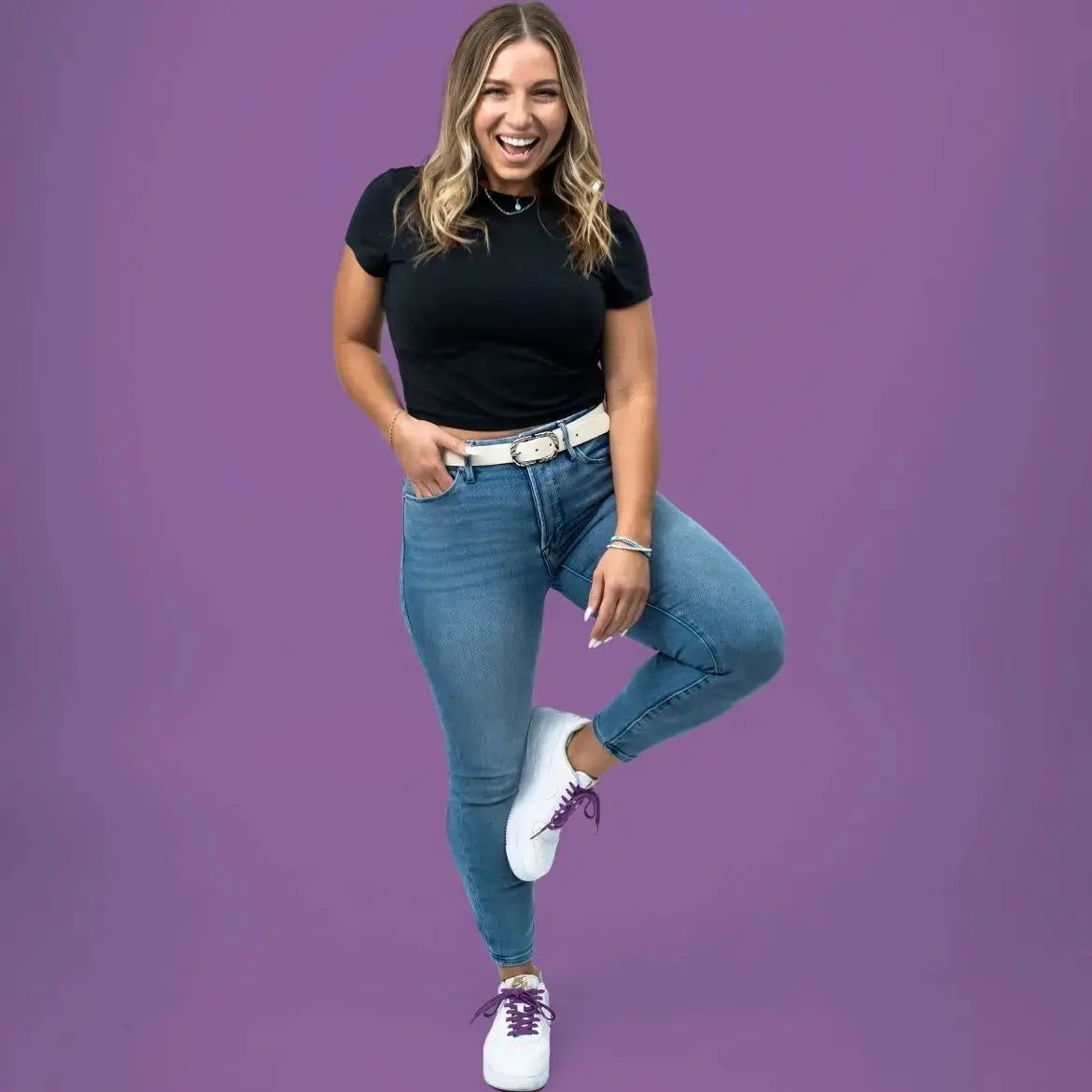 Woman wearing a black top and blue jeans on a purple background