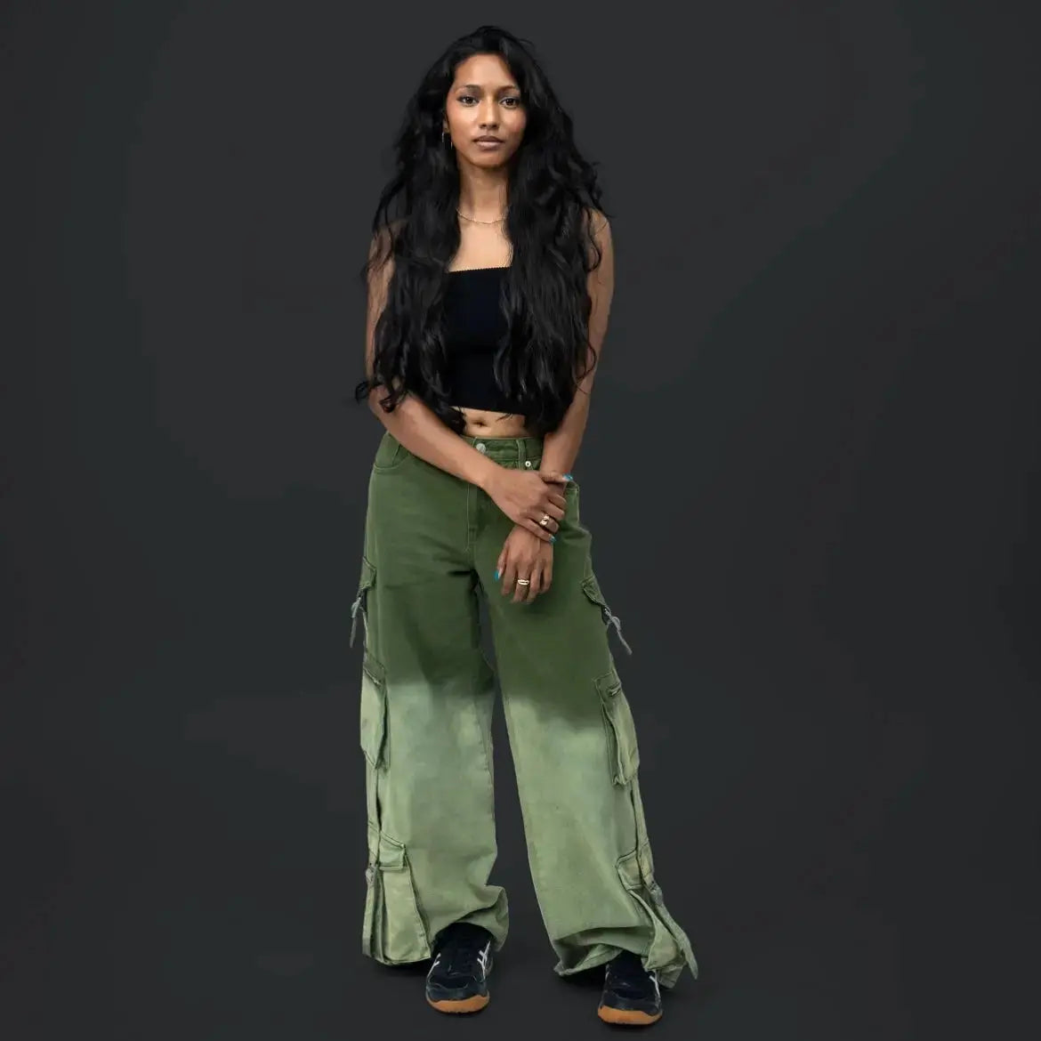 Woman wearing green cargo pants and a black top on a dark background
