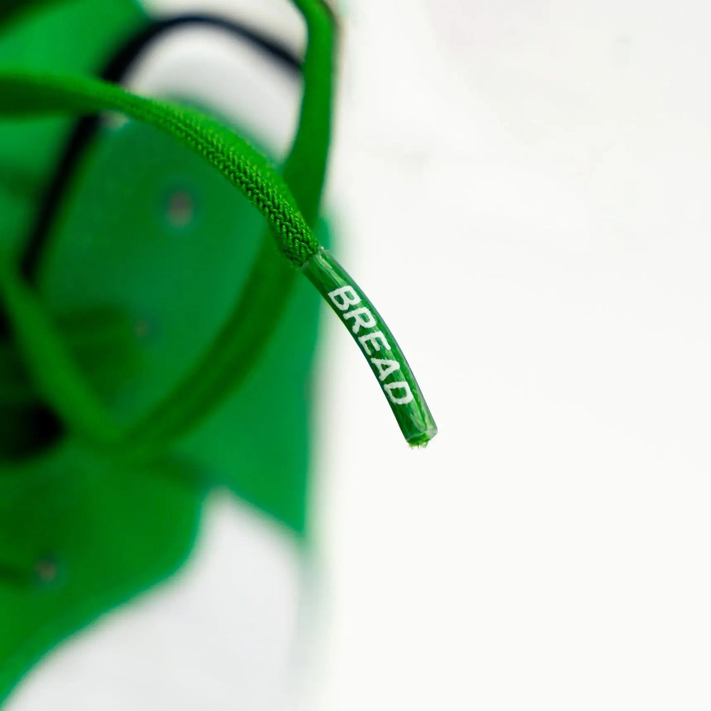 Close-up of green shoelace with 'BREAD' branding on a blurred background