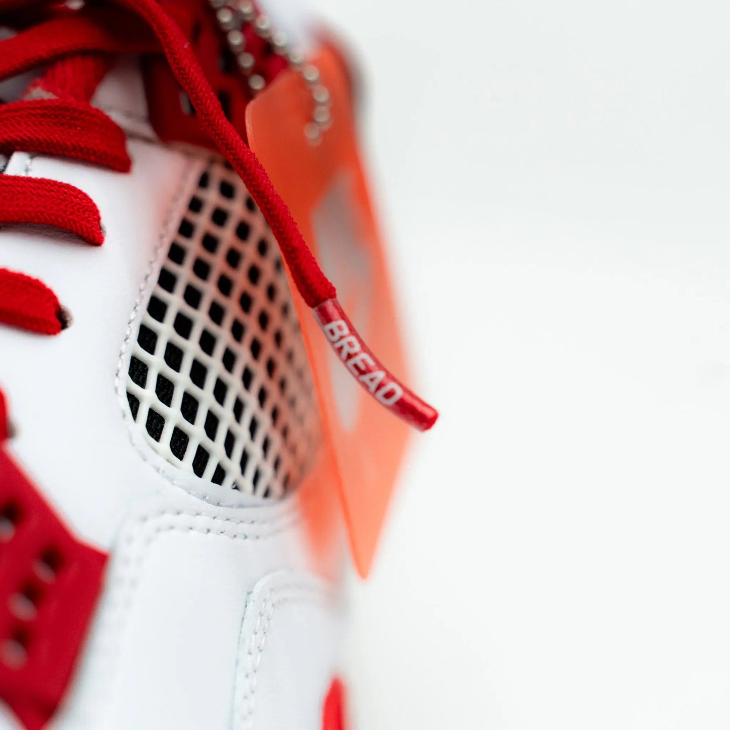 Close-up of a white sneaker with red laces and orange tag on a white background