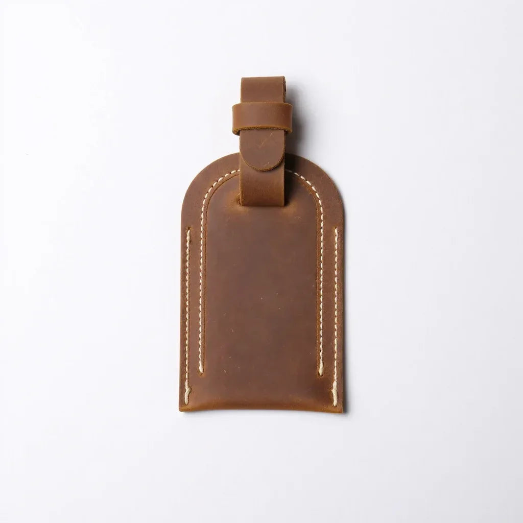 Front view tan full grain leather luggage tag with metal buckle and vertical stitched lines.