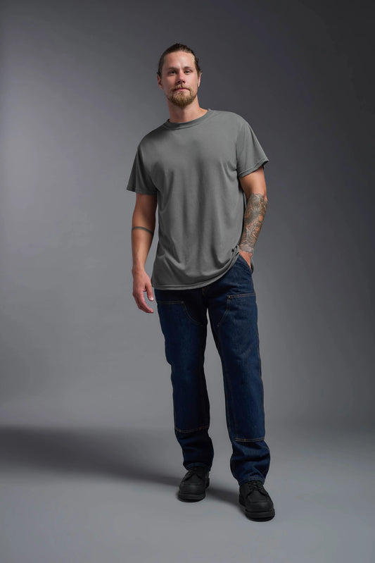 Man wearing a gray t-shirt and blue jeans standing against a gray background